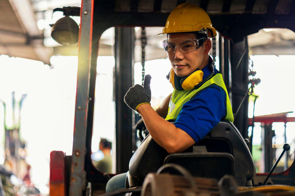 A male employee driving a forklift and showing thumb up in factory.