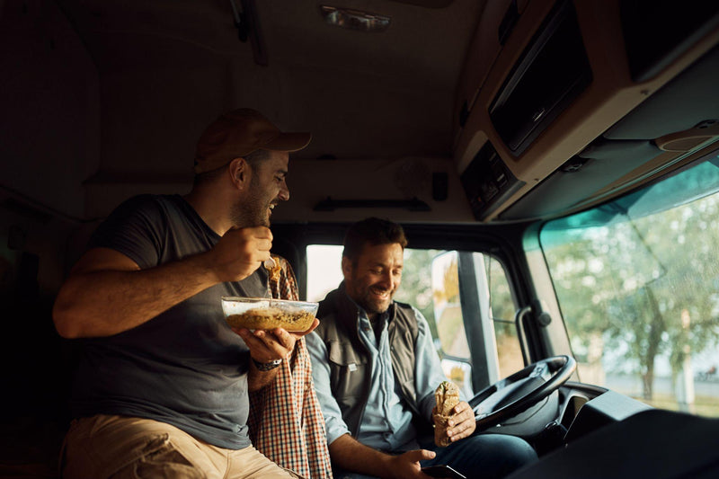 Happy drivers eating on lunch break in truck cabin on parking lot.