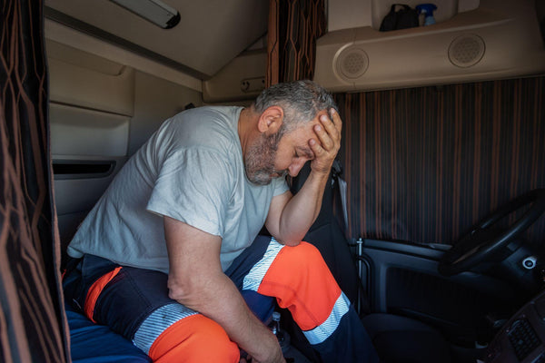 Senior trucker sitting in the bed of the truck with the curtains drawn with a worried gesture