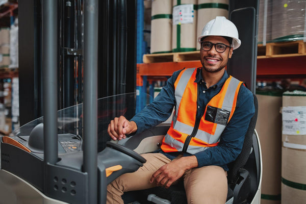 Smiling forklift driver with spectacles sitting in vehicle in warehouse