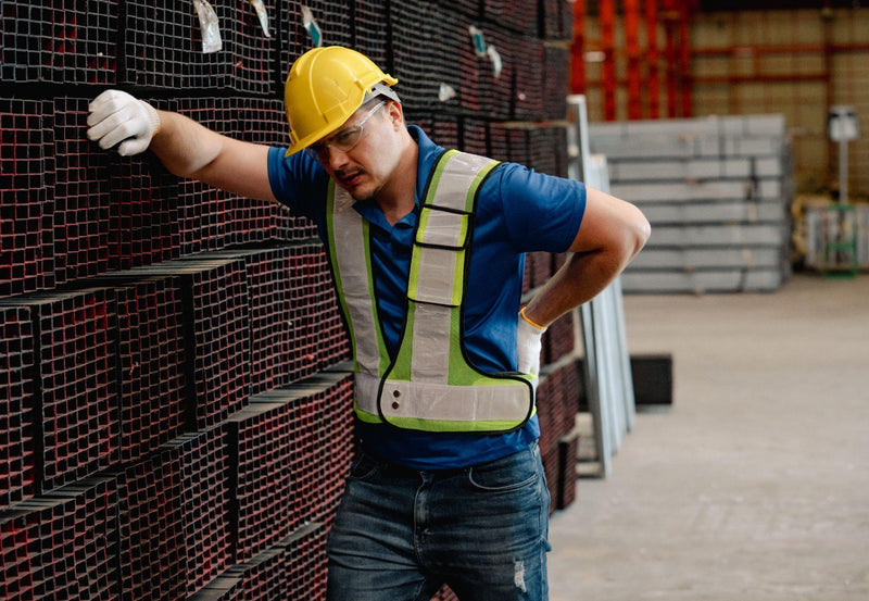 A forklift driver in a warehouse holding his back as if he is in pain