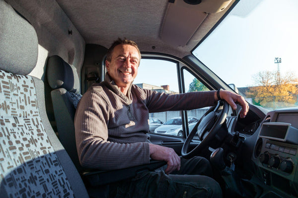 A man driver is sitting in the cab of a truck. 