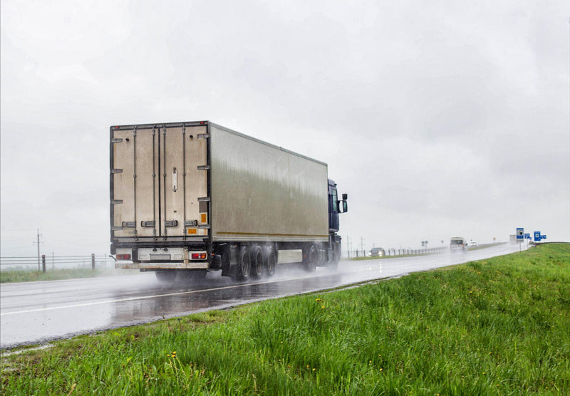 A truck with a semitrailer transports cargo in poor visibility on the road, rain.