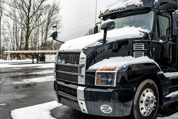 Black big rig semi truck standing on the winter truck stop parking lot with snow and ice