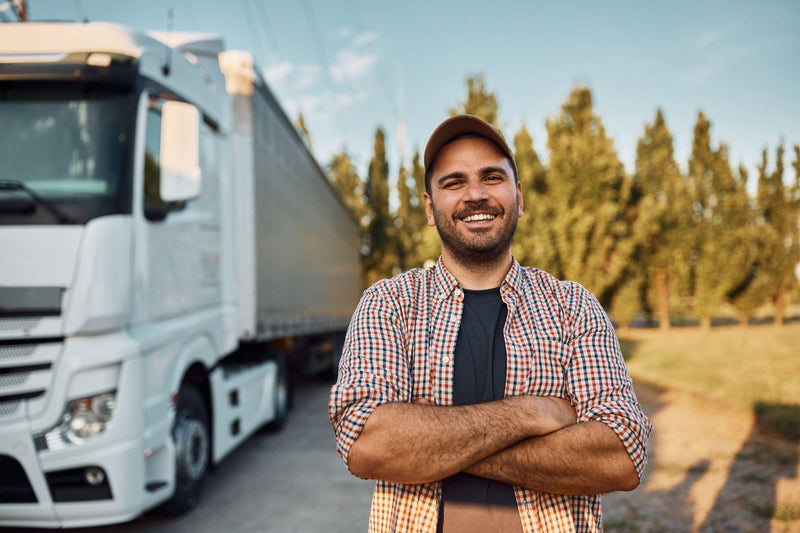 Happy truck driver with crossed arms standing on parking lot and looking at camera.