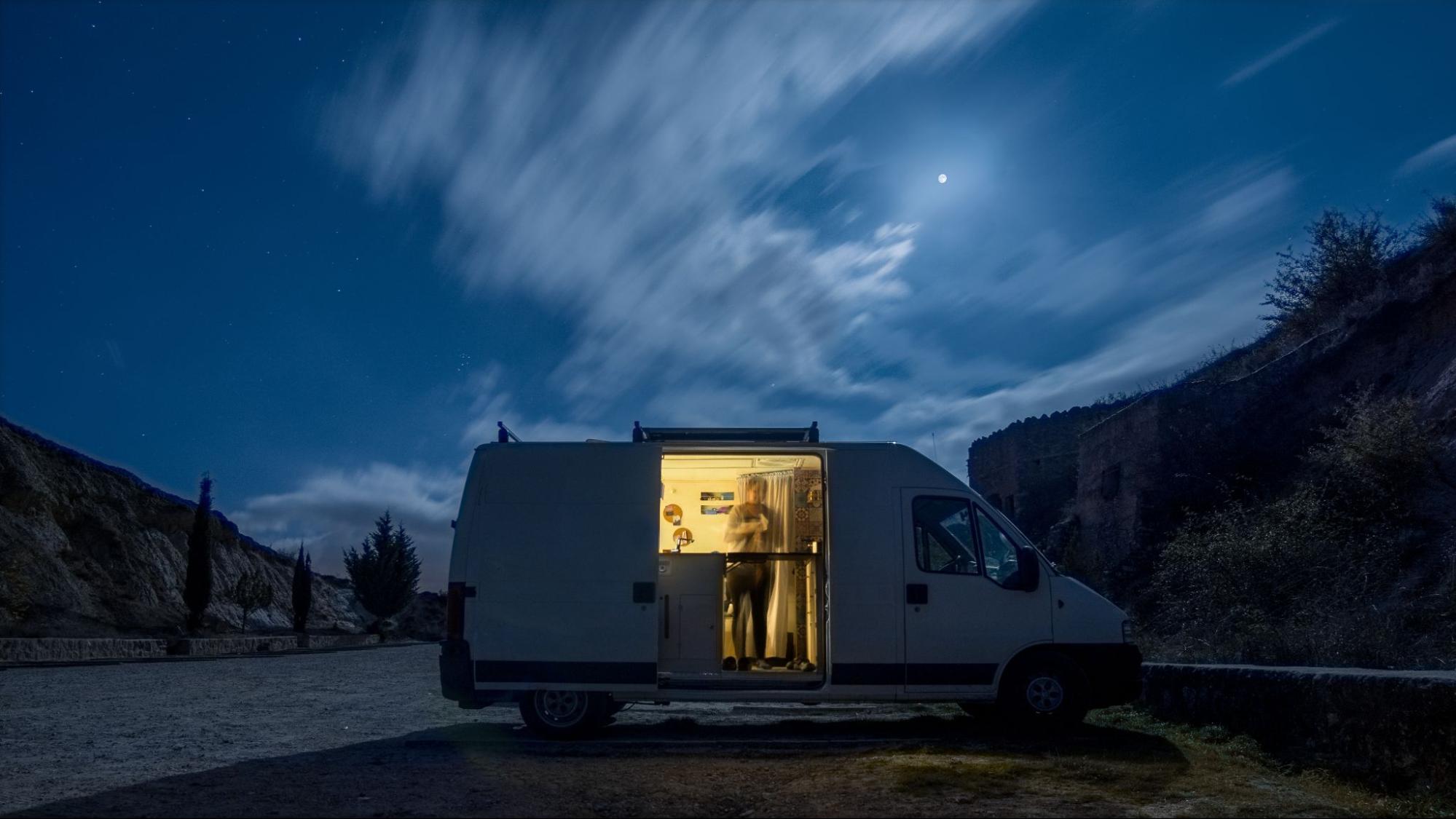 A person standing in their camper van with the light on at night