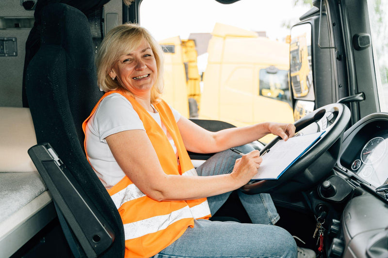 Mature woman truck driver steering wheel inside lorry cabin.