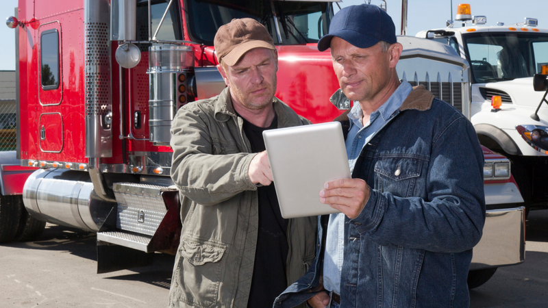two truck drivers using a tablet PC in front of trailers.